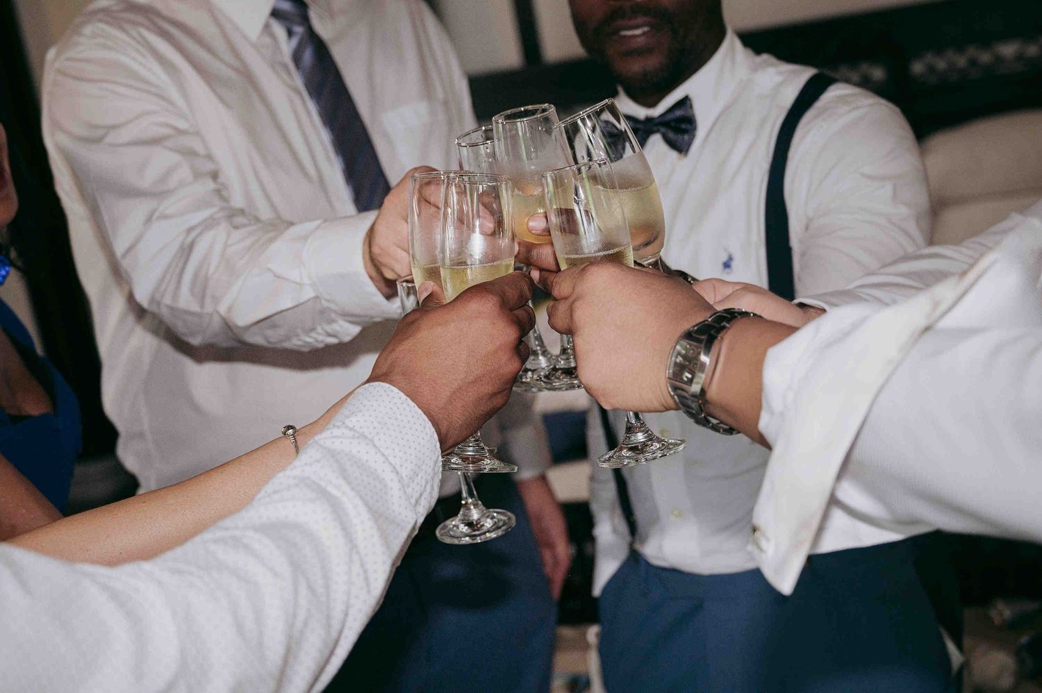 Groomsmen in white shirts and suspenders toasting with champagne glasses at a wedding celebration.