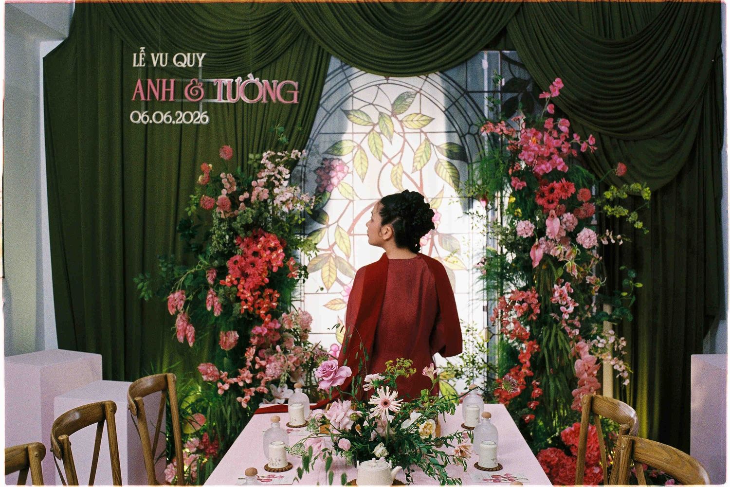 A woman in red stands before a floral wedding backdrop at a Vietnamese Vu Quy ceremony on 06-06-2025.