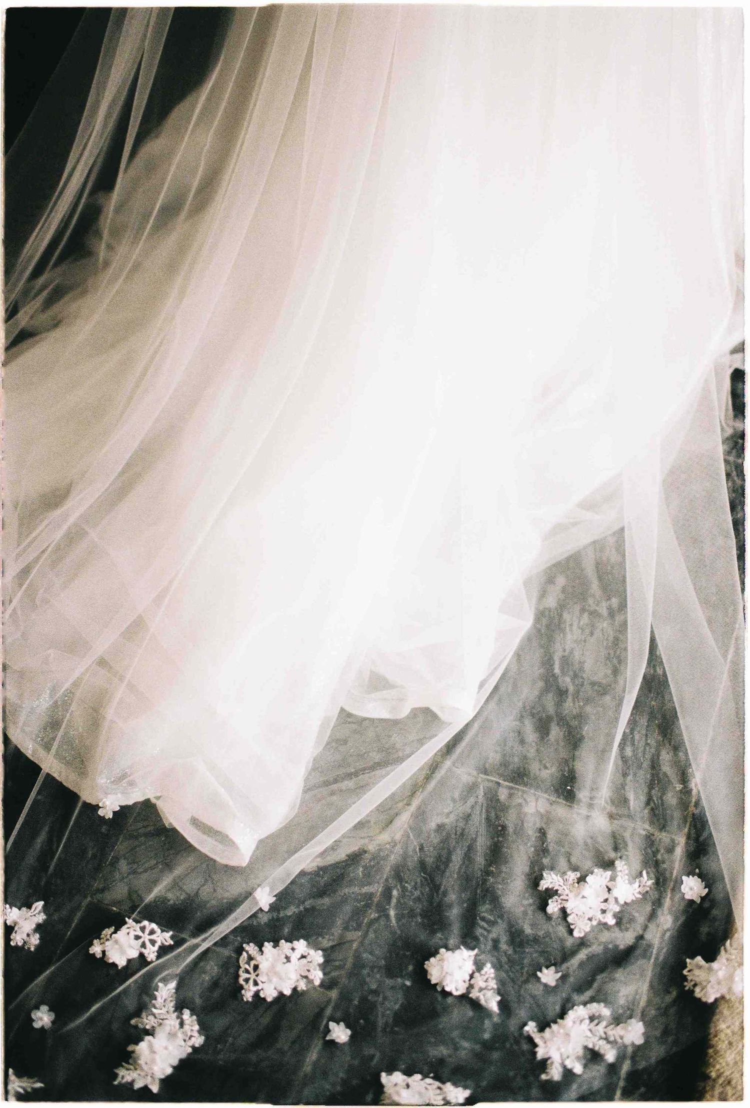 Flowing white bridal veil draped over dark surface with delicate floral details, elegant wedding photography.