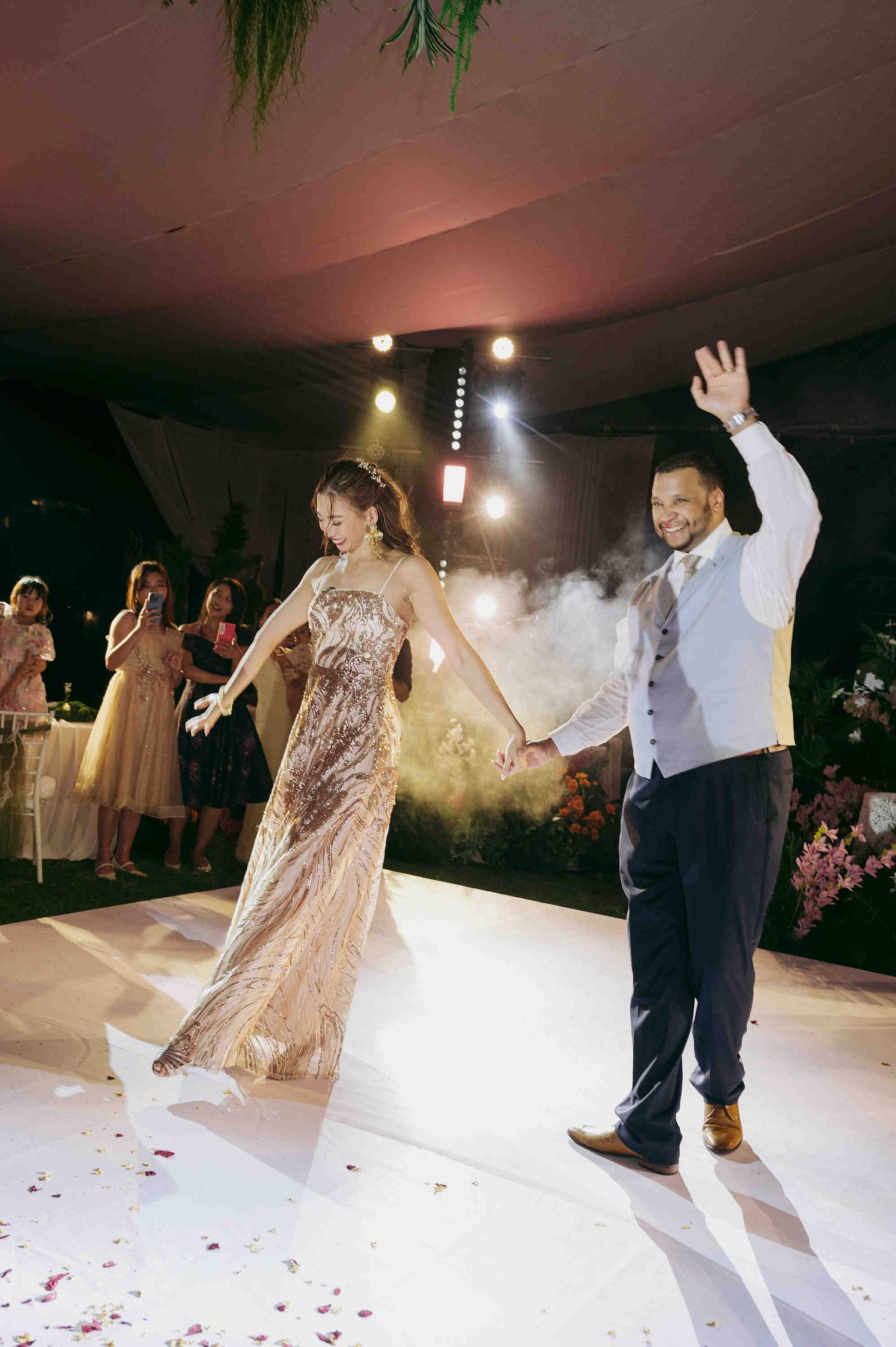Bride and groom make grand entrance on white dance floor at elegant wedding reception with stage lighting.