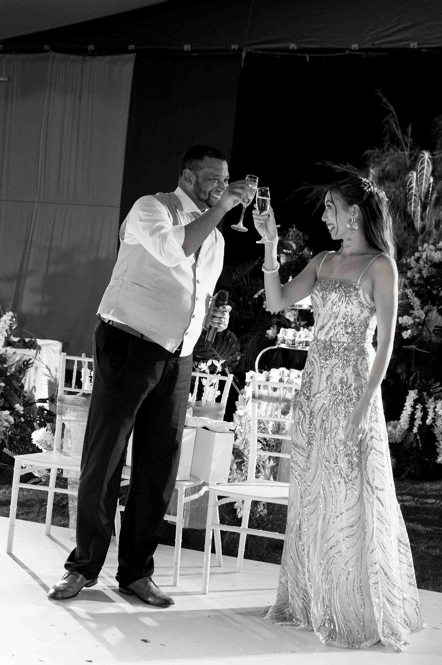 Black and white photo of a couple toasting with champagne glasses at an elegant outdoor wedding reception.