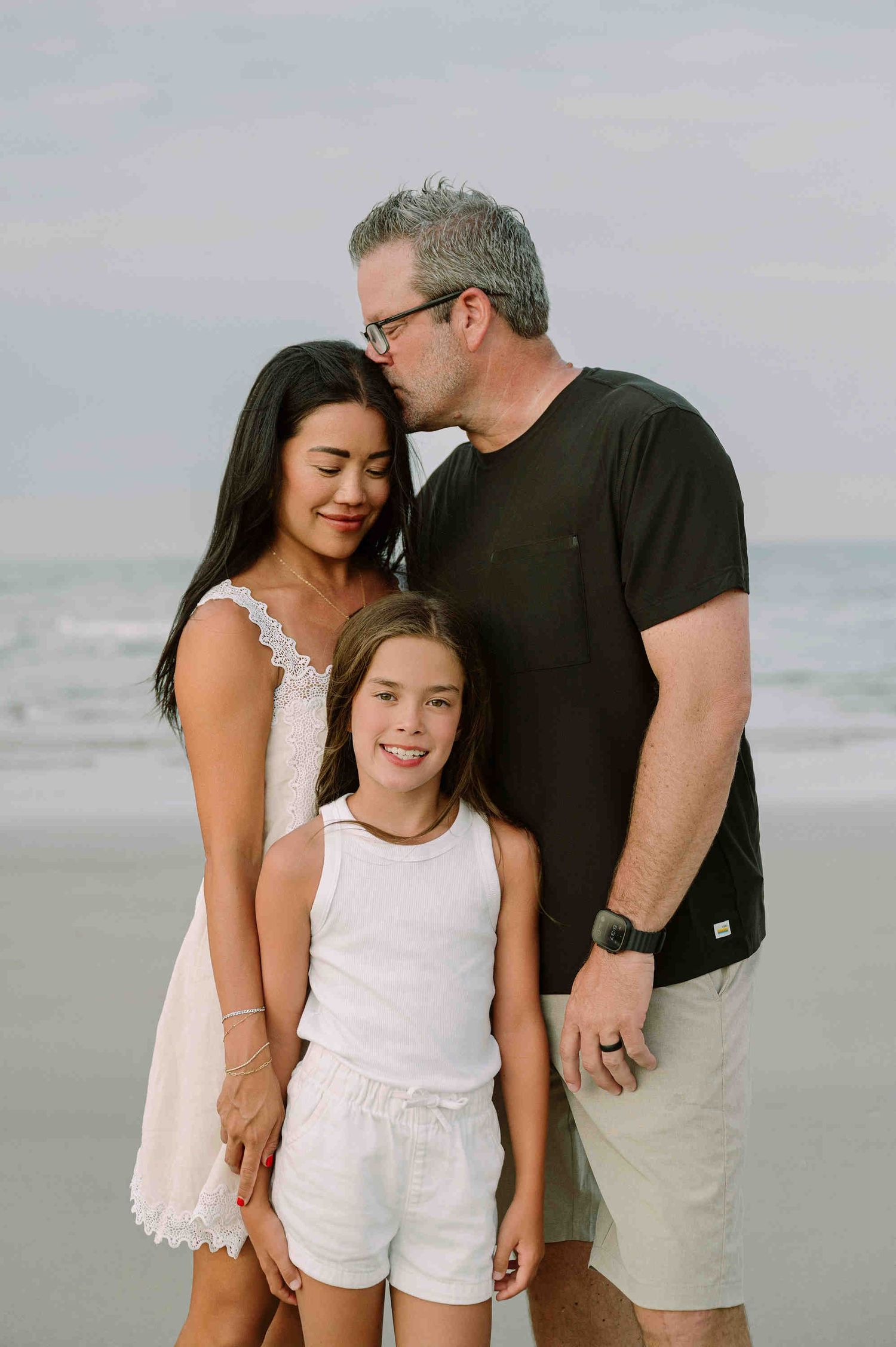 Da Nang family: family of three shares candid moments together on a cloudy beach in matching light-colored outfits, by AnhVuWedding.