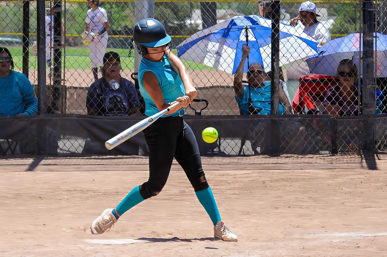 Youth softball batter in teal uniform swings at a pitch during an outdoor league game.