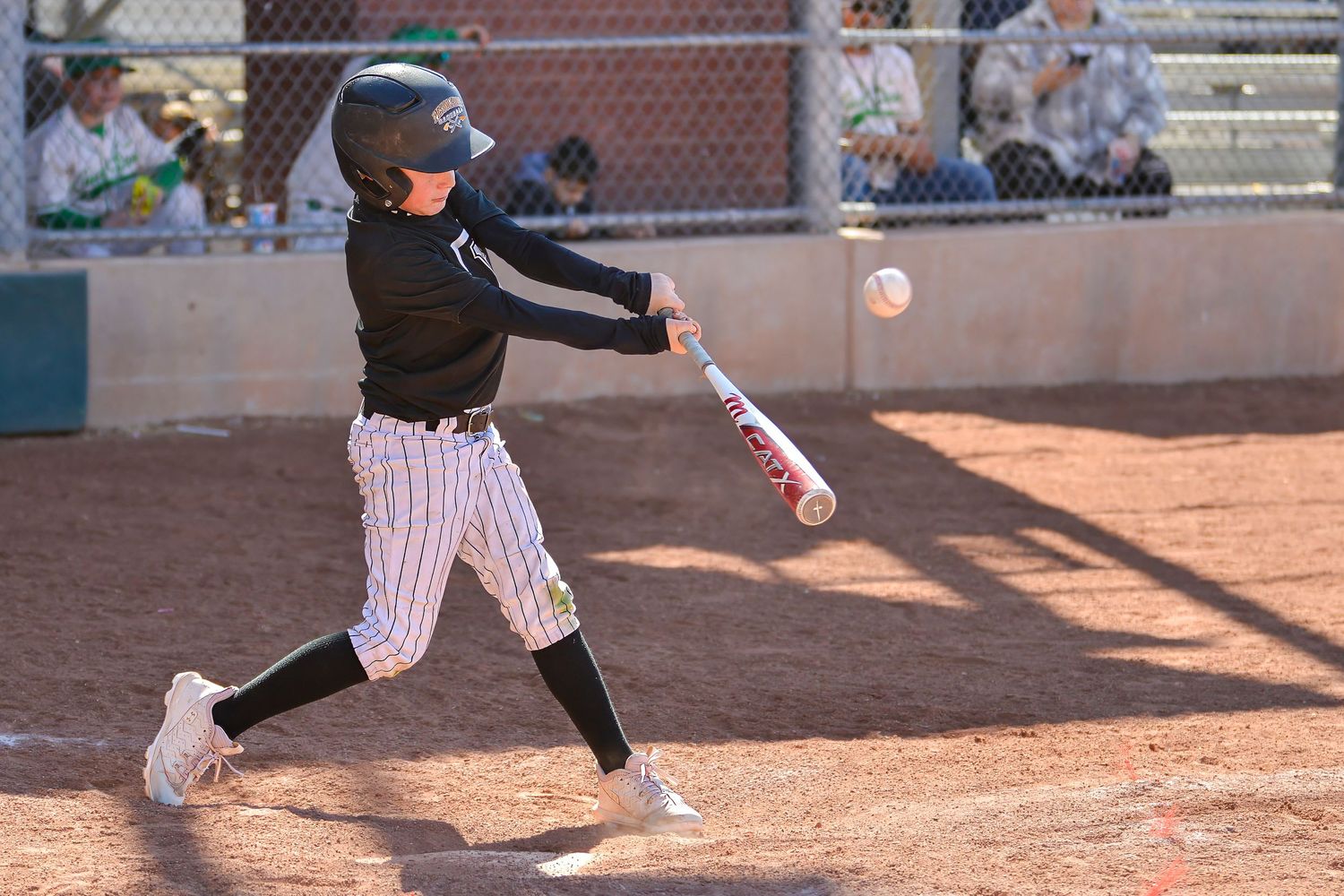 Young baseball batter in black uniform makes contact with the ball during a youth league game.