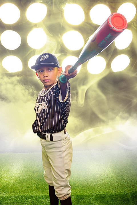 Young baseball player in pinstripe uniform poses with red bat under stadium lights with dramatic smoke effect.