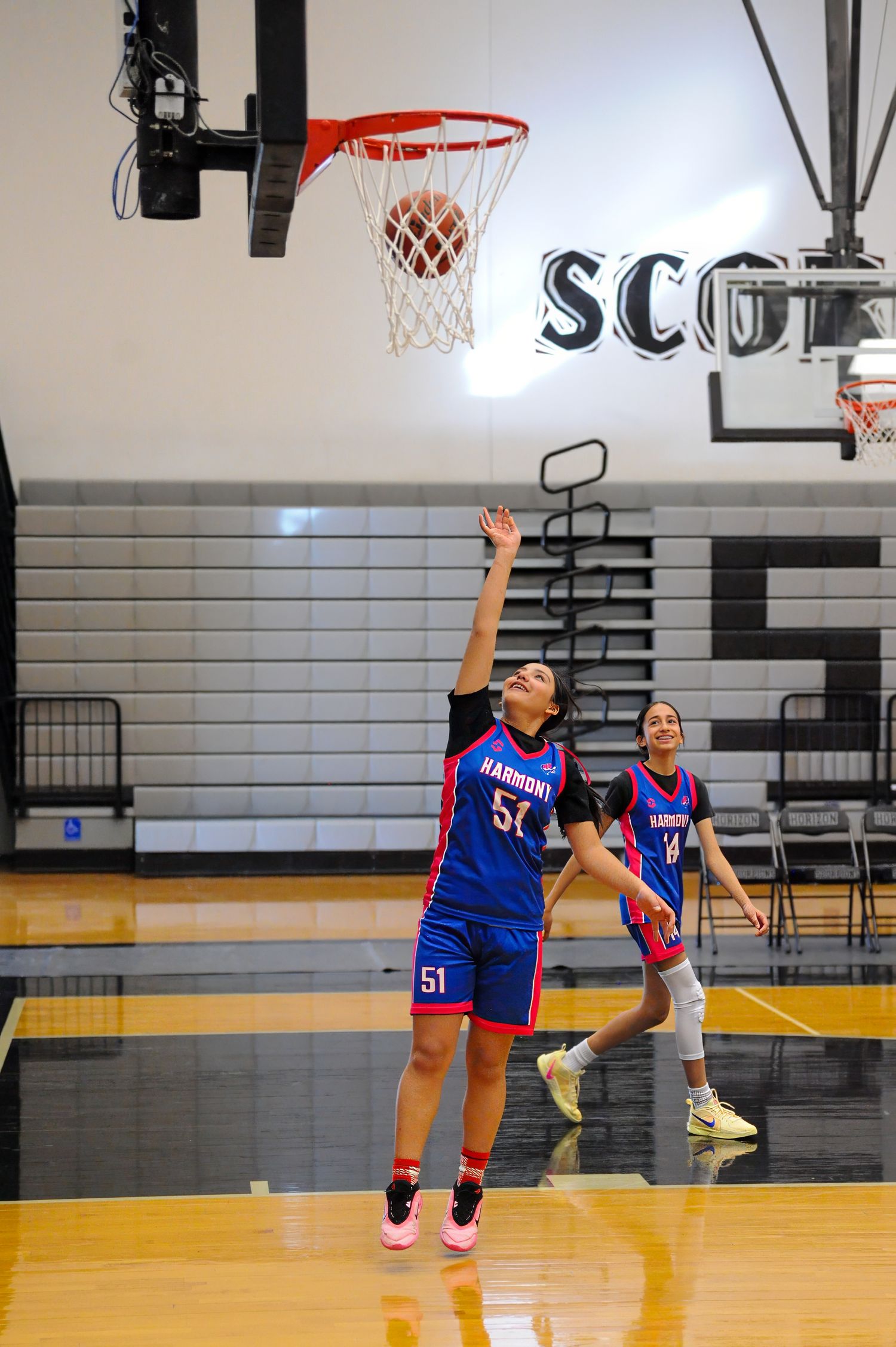 Female basketball player #50 in blue Harmony jersey shoots layup in indoor gym during girls basketball game.