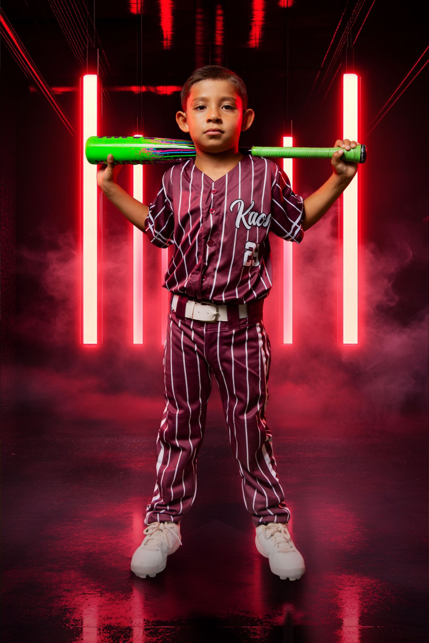 Young baseball player in maroon pinstripe uniform poses with green bat against neon red light background.