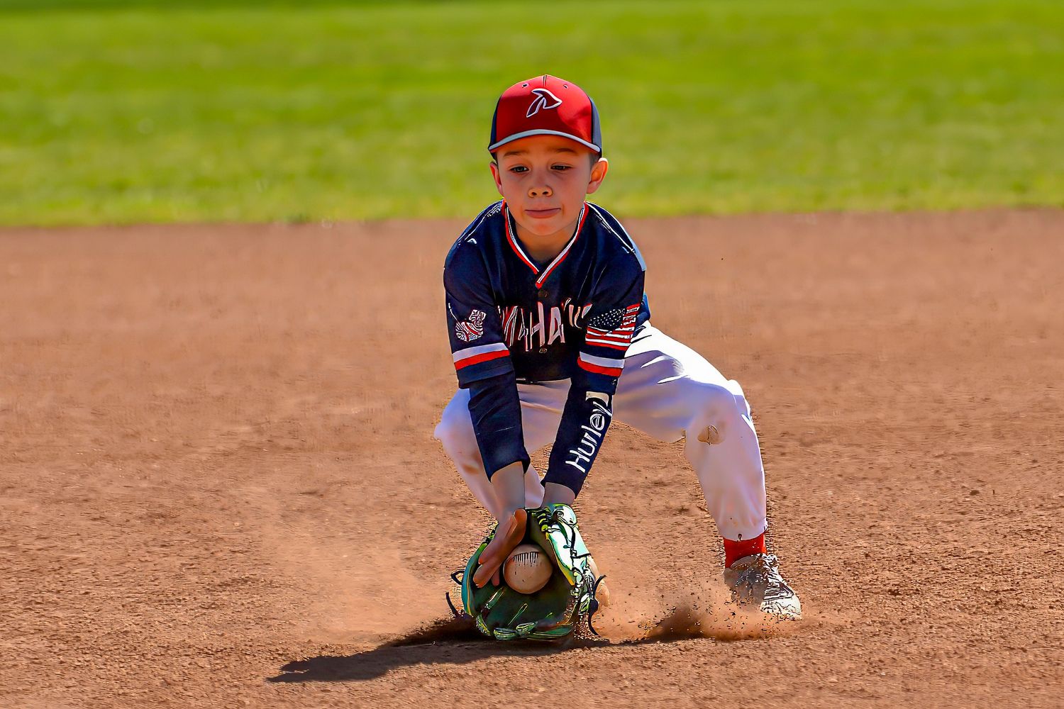 Young baseball infielder fields a ground ball in a crouching position during a youth league game.