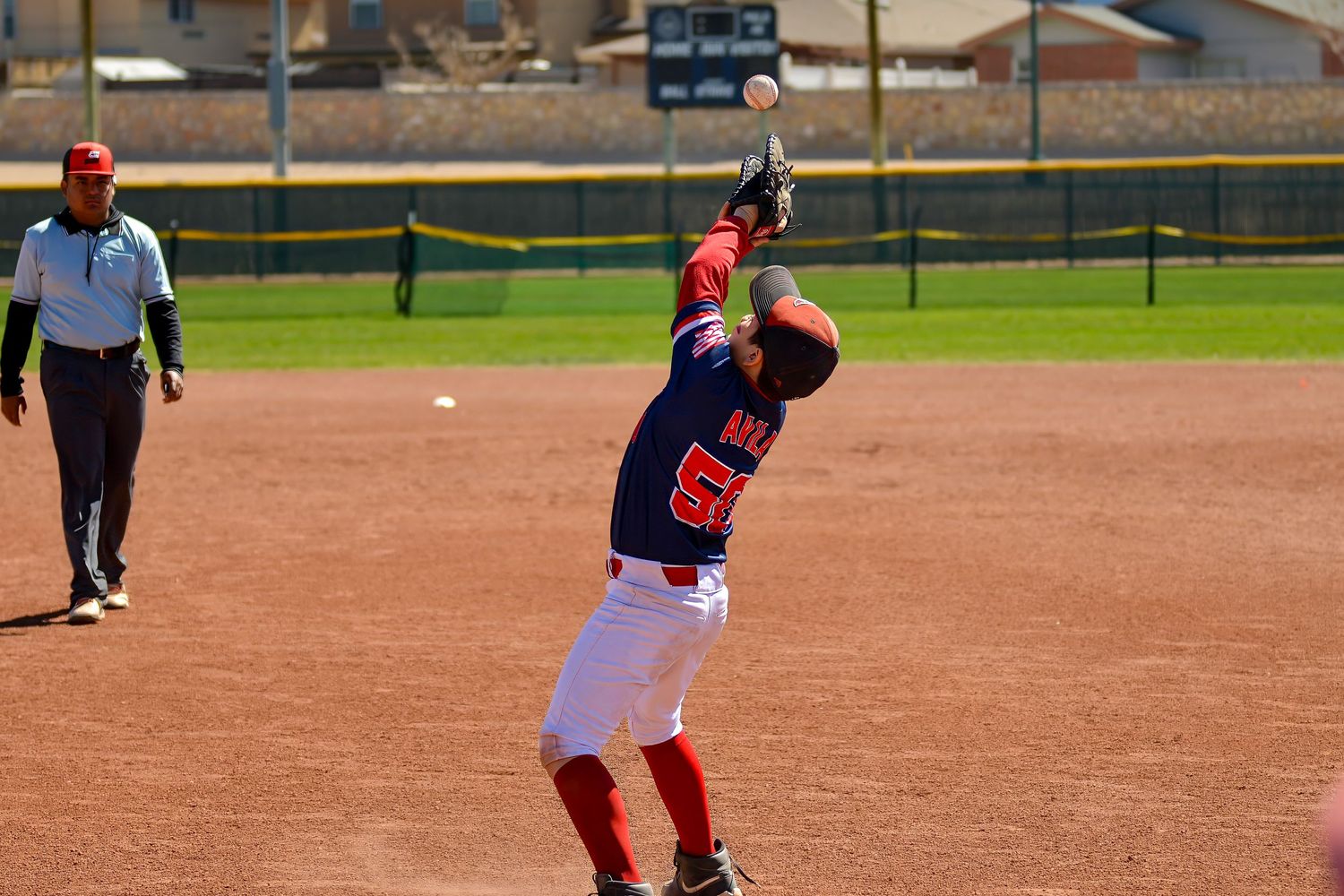 Youth baseball infielder catches a pop fly ball with an umpire watching in the background.