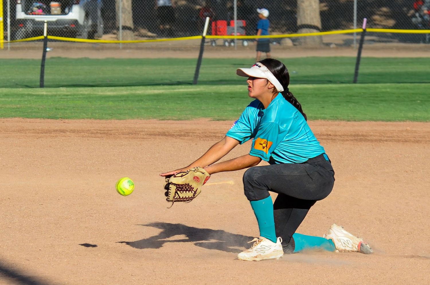 Female softball player crouching low to field a ground ball during a competitive game on a dirt infield.