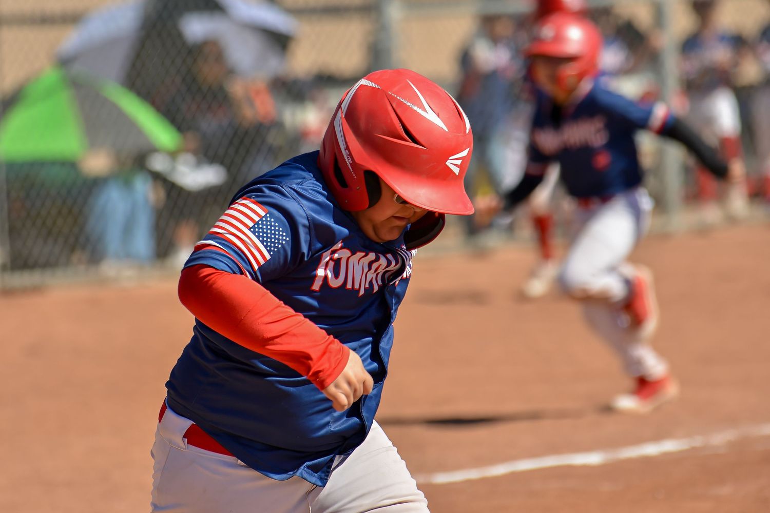 Young baseball player in red helmet and blue uniform sprinting the bases during a youth league game.