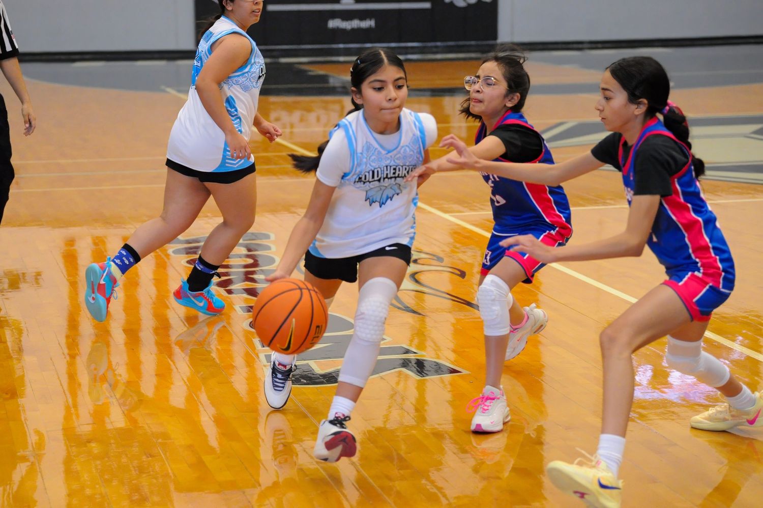 Young girls playing competitive basketball game, dribbling and defending on indoor court.