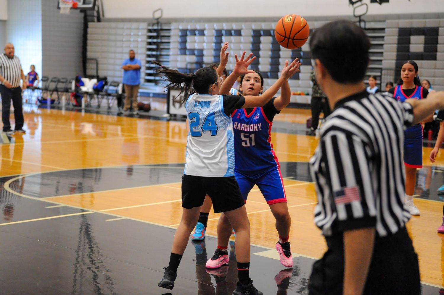 Young girls playing youth basketball game, player #51 in blue attempts shot against defender #24 in white gym.
