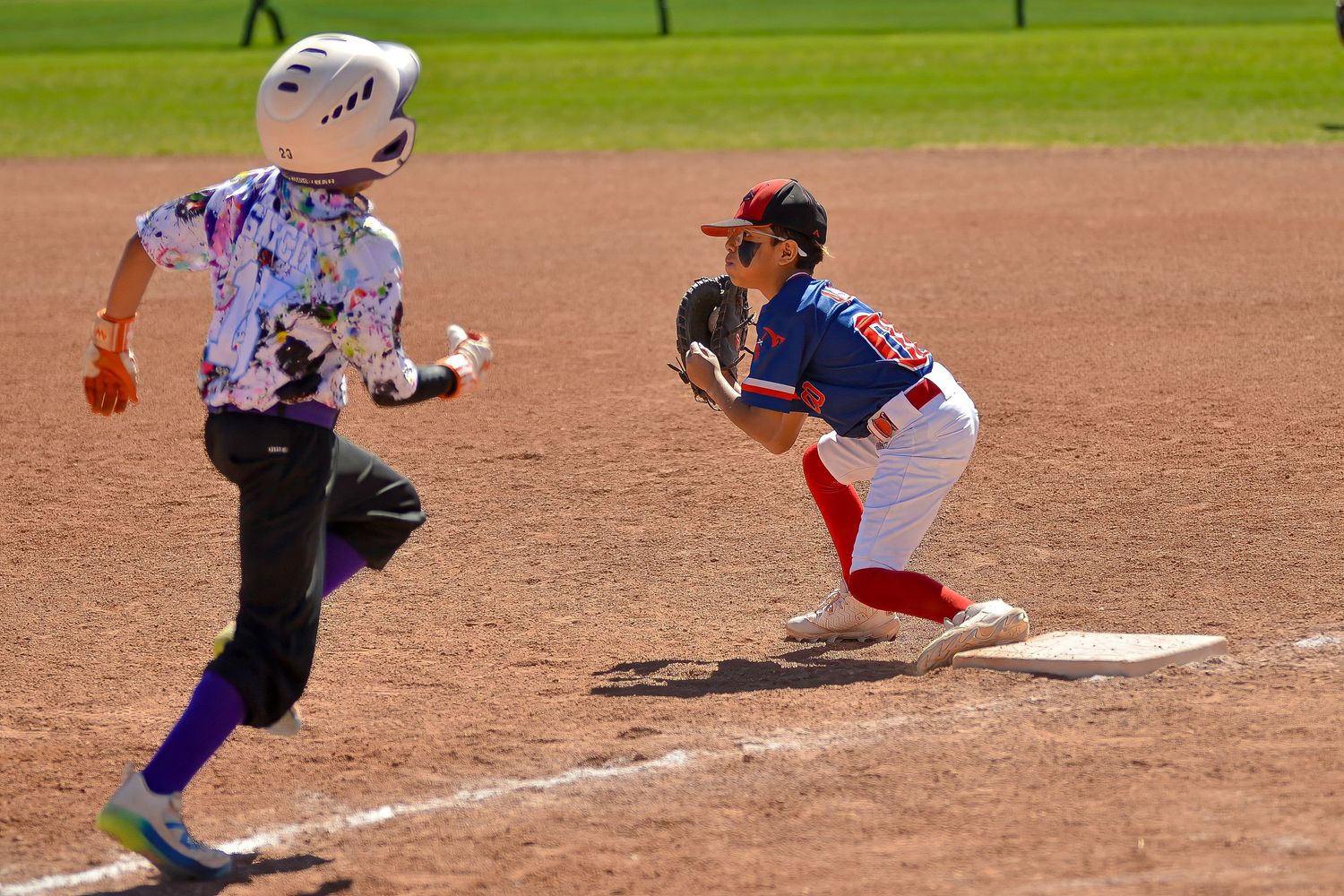 Youth baseball first baseman catches the ball to record an out during a little league game.