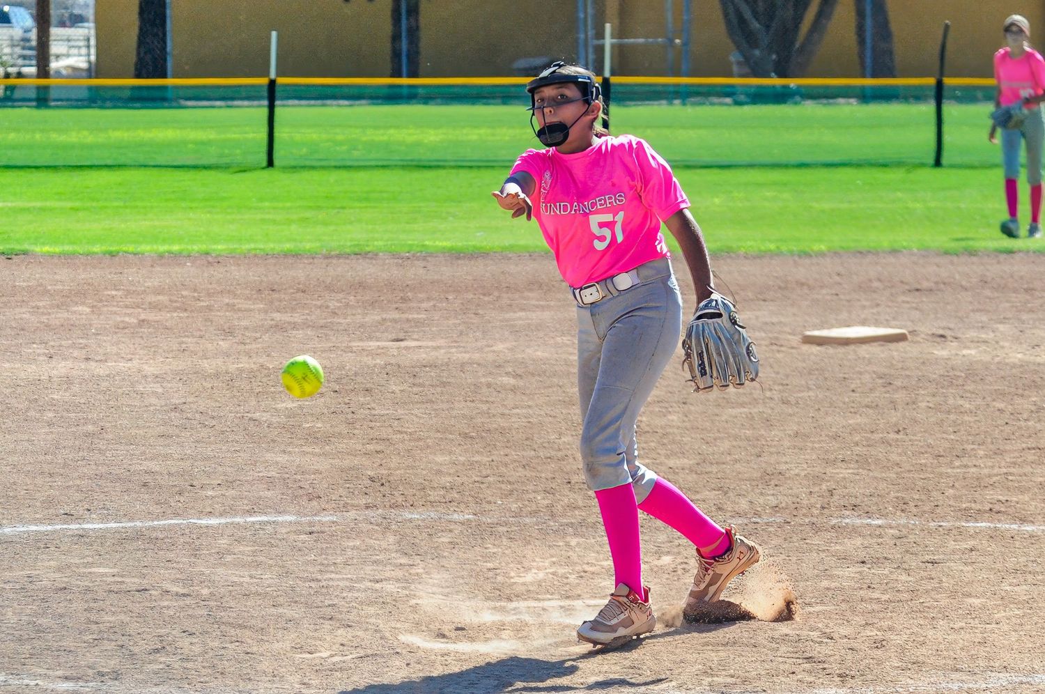 Female softball pitcher wearing number 51 in pink uniform releasing a pitch during an outdoor game.