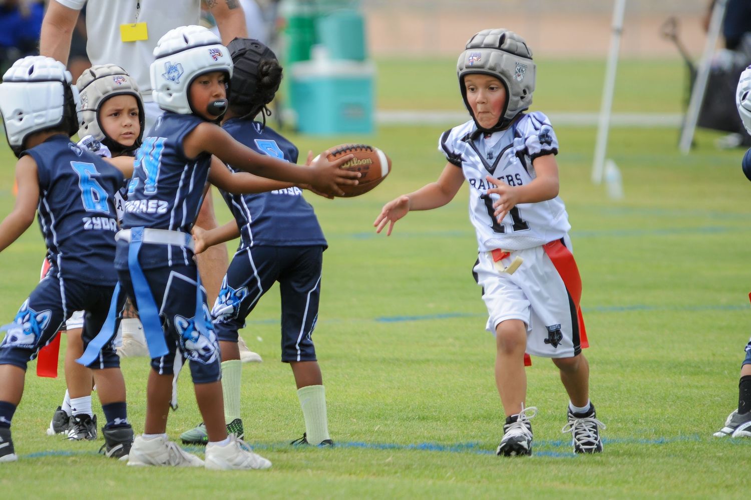 Young children playing youth football in helmets, with one player carrying the ball during a game.