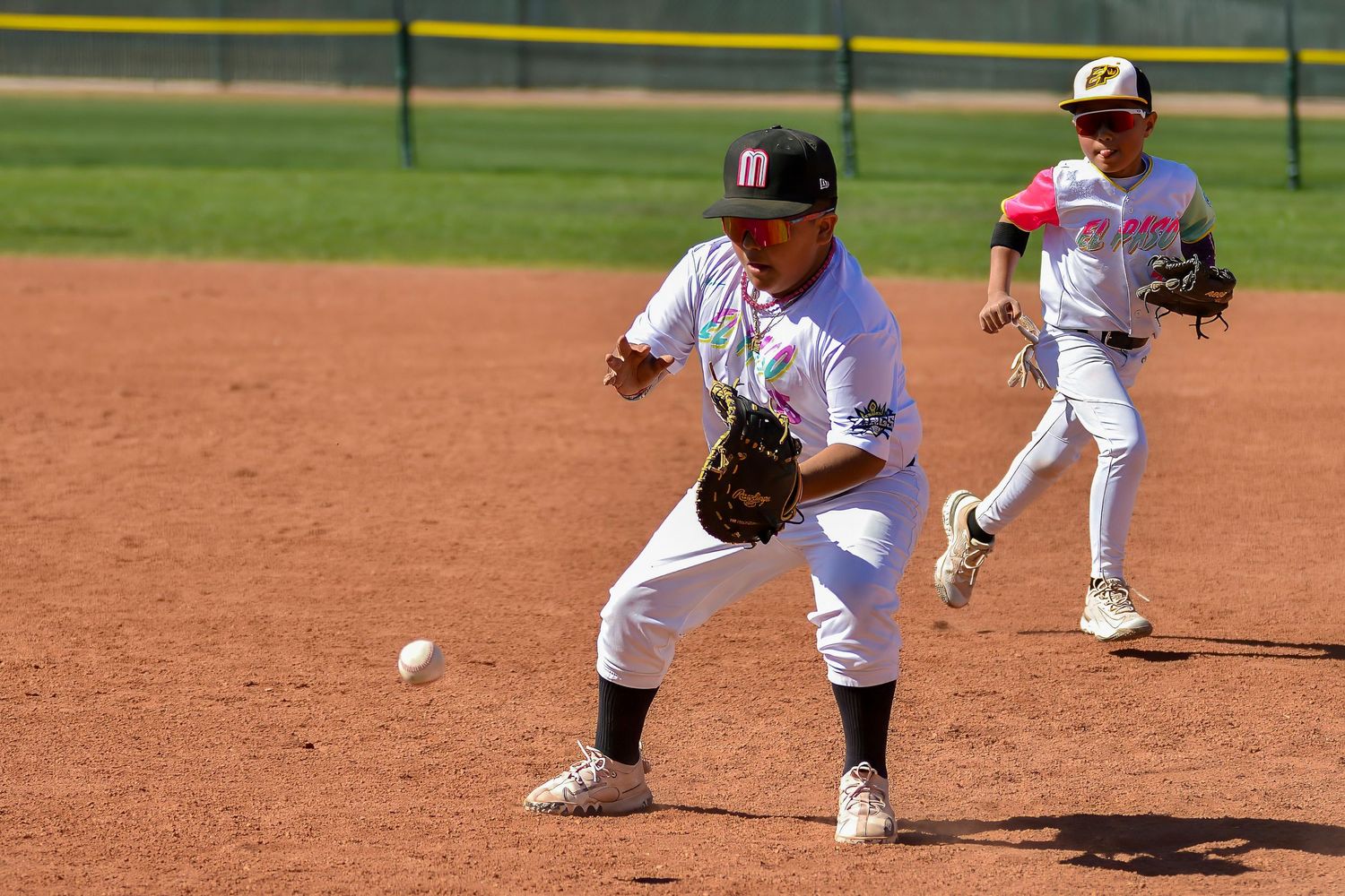 Youth baseball infielder fields a ground ball while teammate backs up the play during a game.