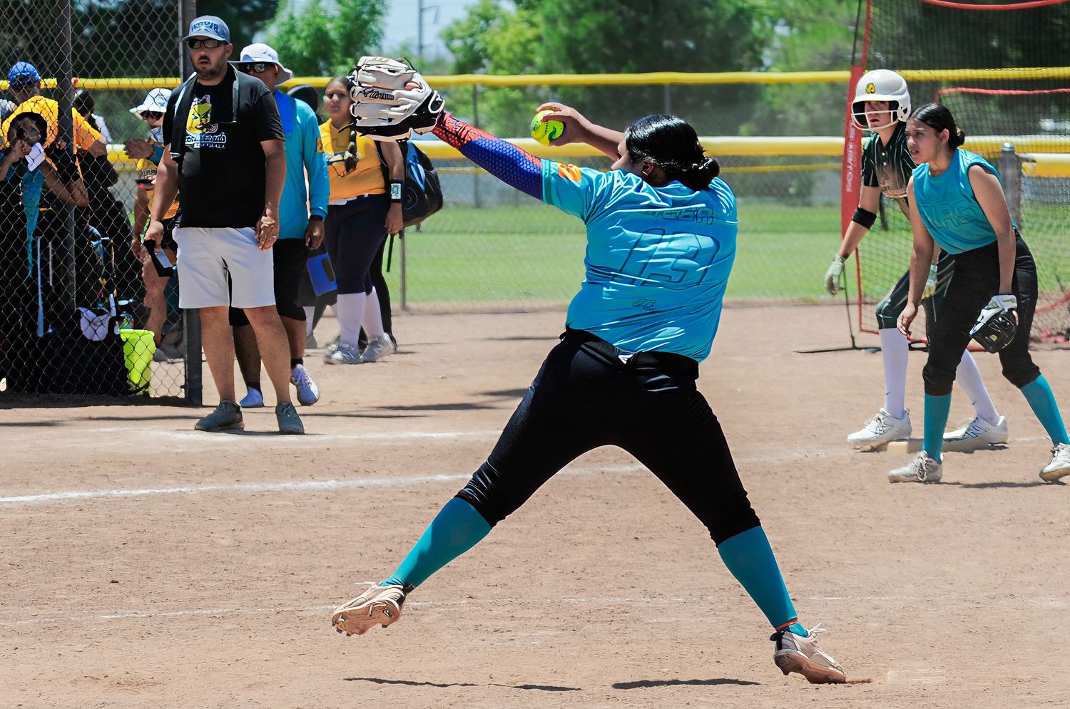 Youth softball pitcher winds up for an underhand pitch during a competitive outdoor league game.