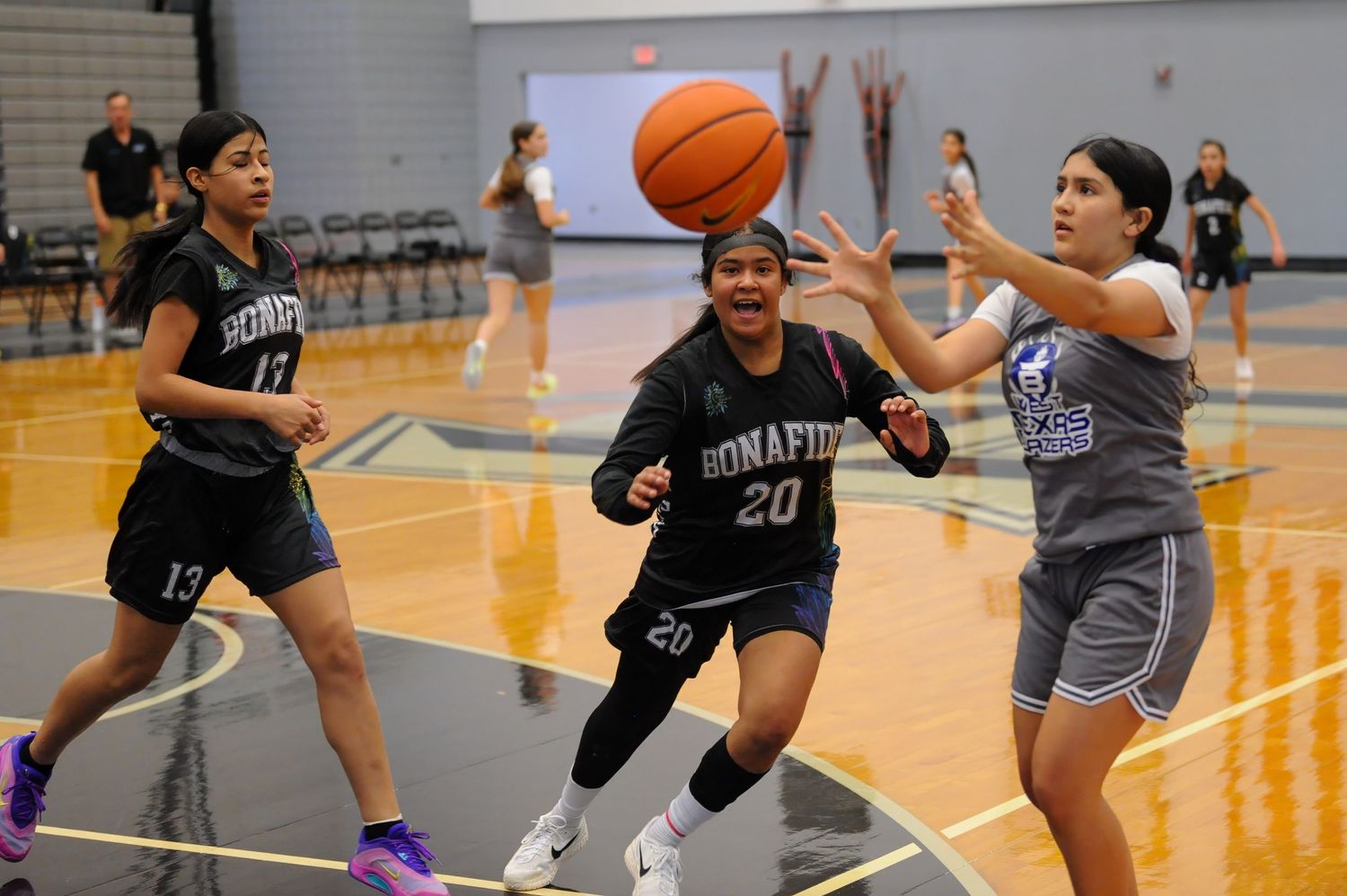 Girls basketball players compete for a loose ball during a Bonafide team practice in a school gymnasium.