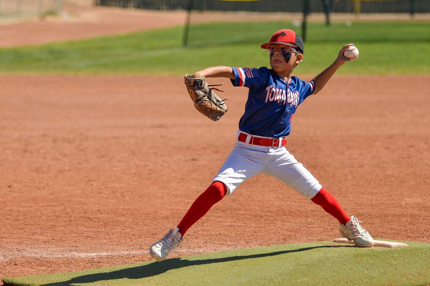 Young baseball pitcher in red uniform winds up to throw during a youth league game on a sunny day.
