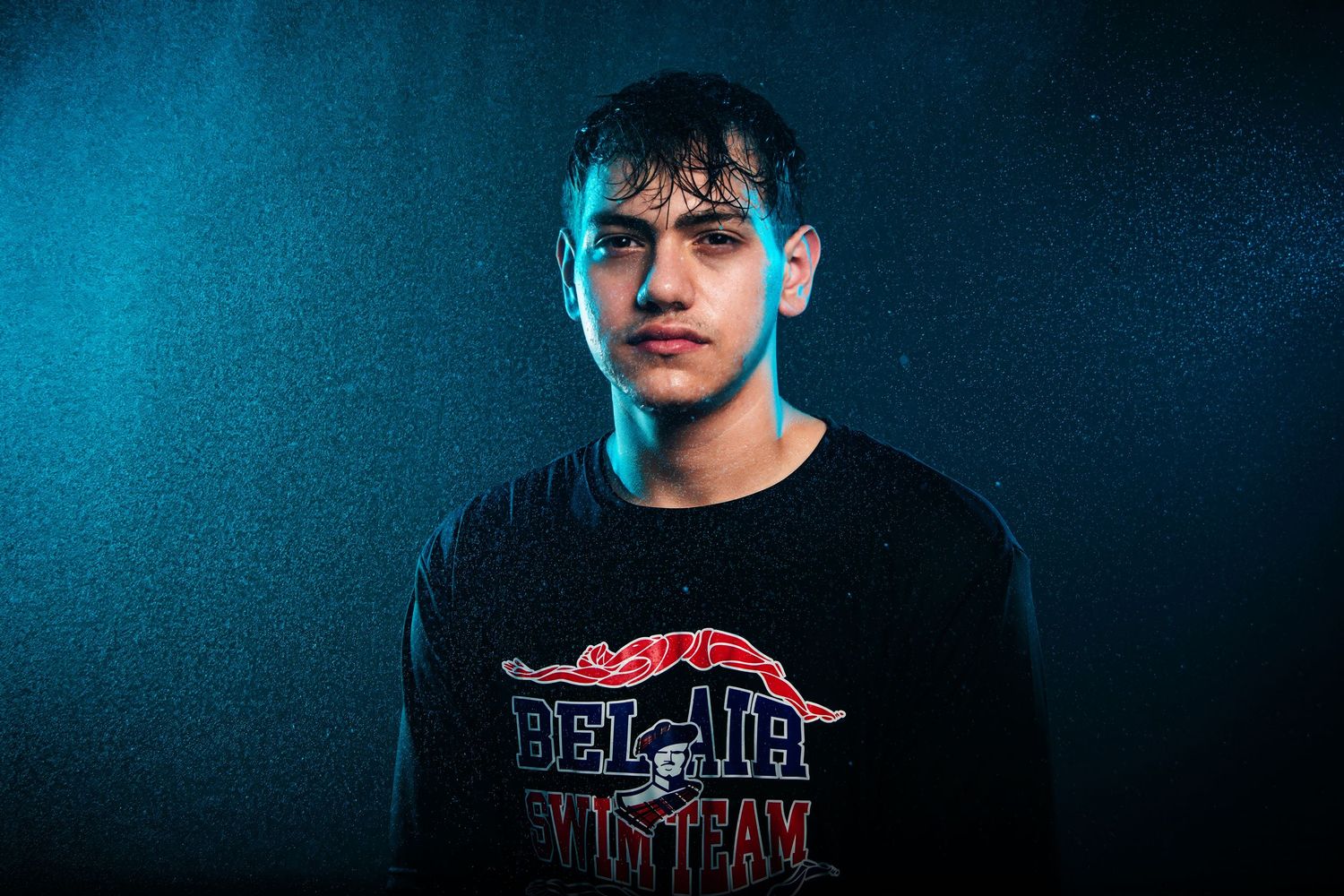 Teen boy in Bel-Air Vietnam black tee poses under blue and white studio lighting with rain effect backdrop.