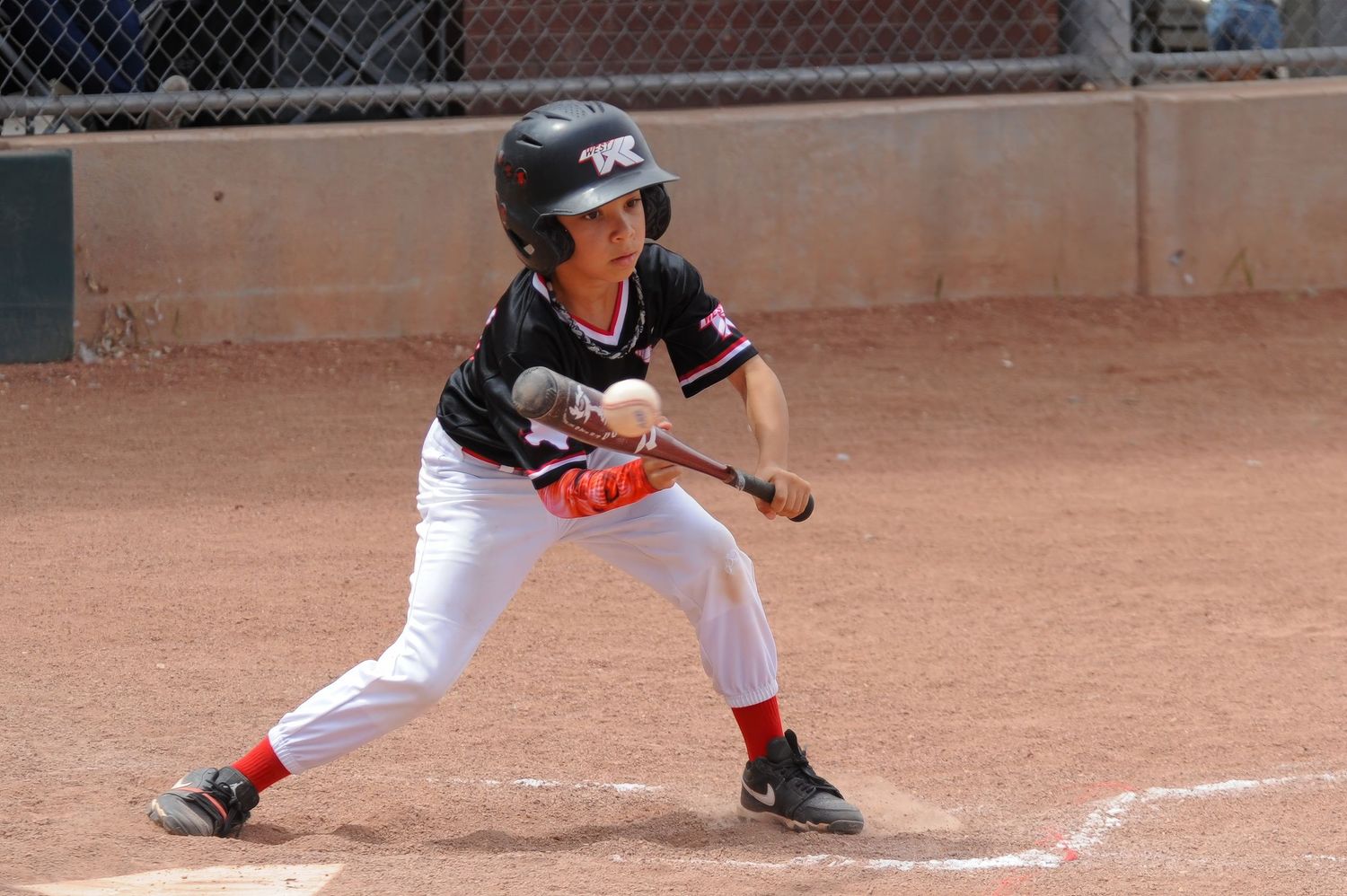 Young baseball player in black helmet and uniform prepares to bunt at home plate during a youth game.