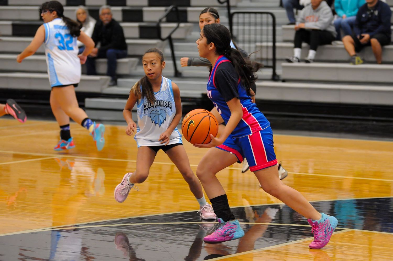 Two girls playing basketball in a gym, one dribbling past a defender during a youth basketball game.