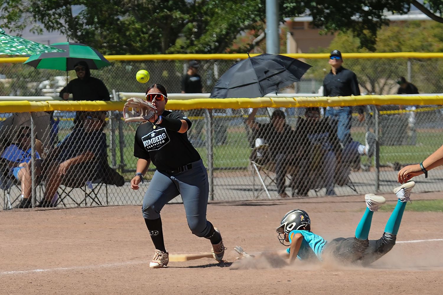 Softball player reaches for a throw as opponent slides into base during a competitive youth game.