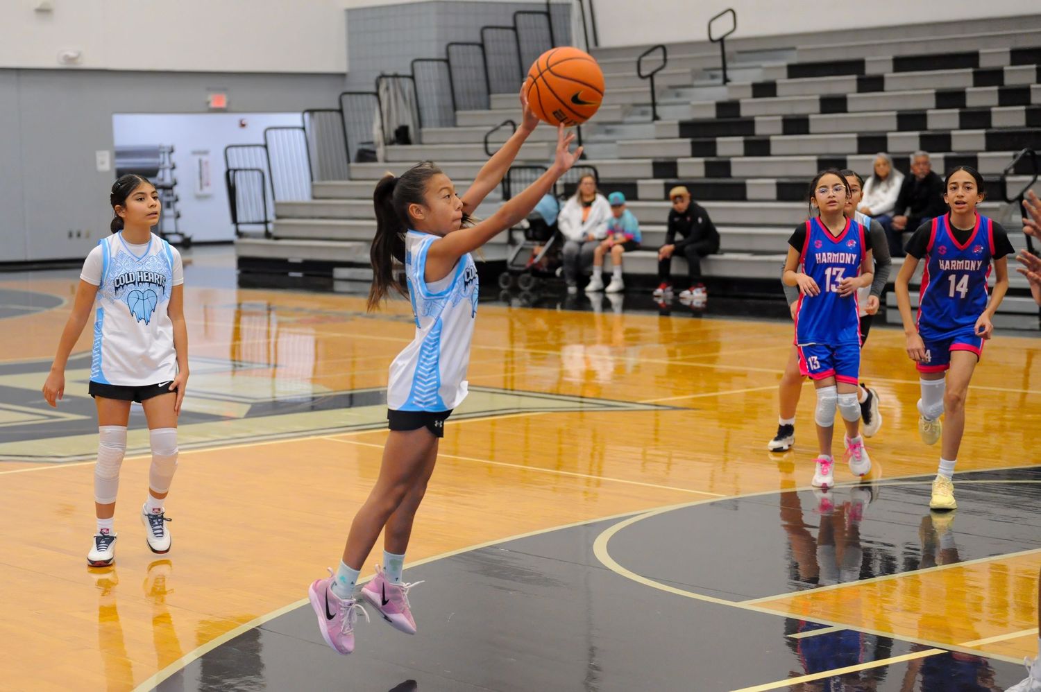 Young girl in light blue jersey shoots a basketball during a girls youth basketball game in an indoor gymnasium.