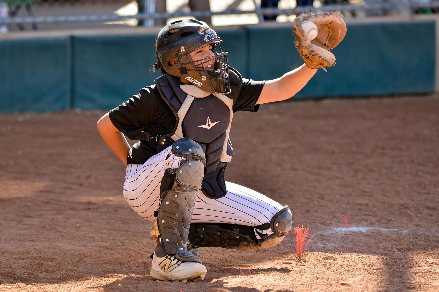 Young baseball catcher in full gear crouches to receive a pitch during a youth league game.