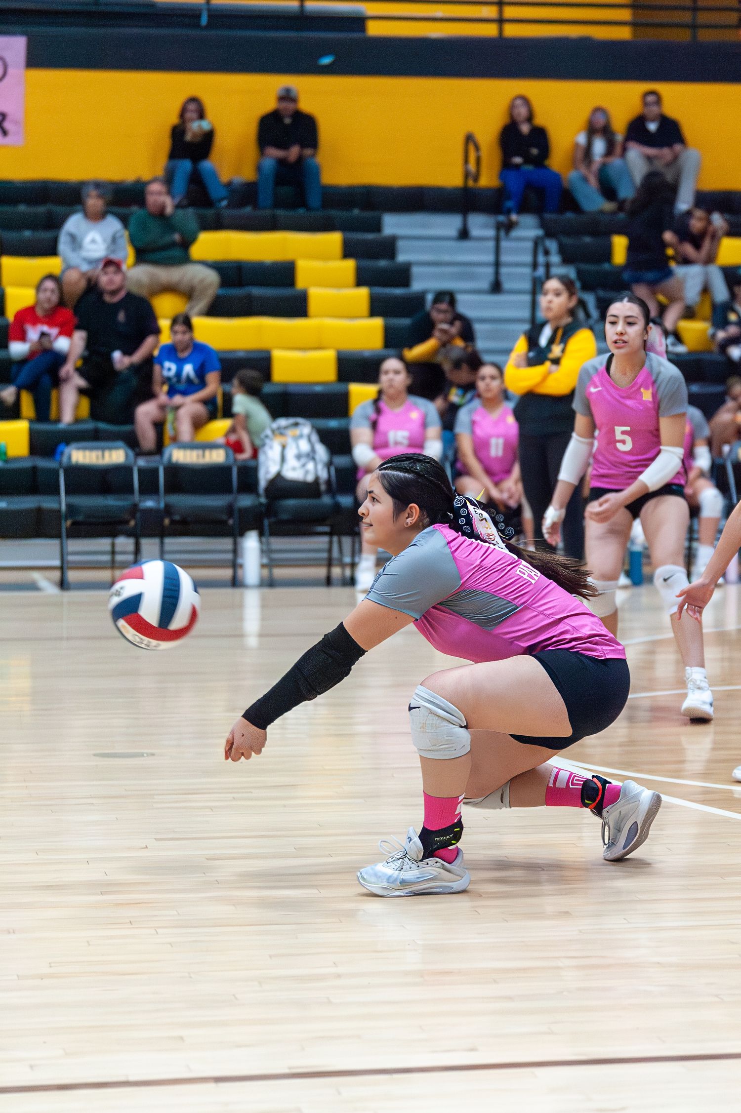 Female volleyball player #10 in pink uniform dives low to dig ball during indoor match.
