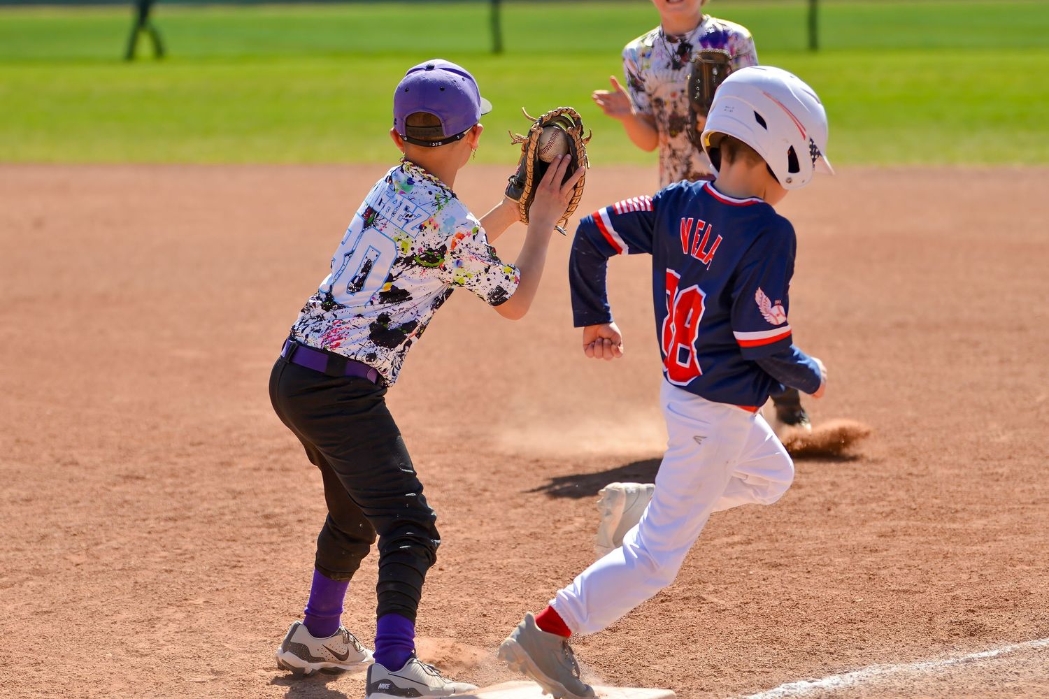 Youth baseball player runs to first base as fielder attempts a tag during a little league game.