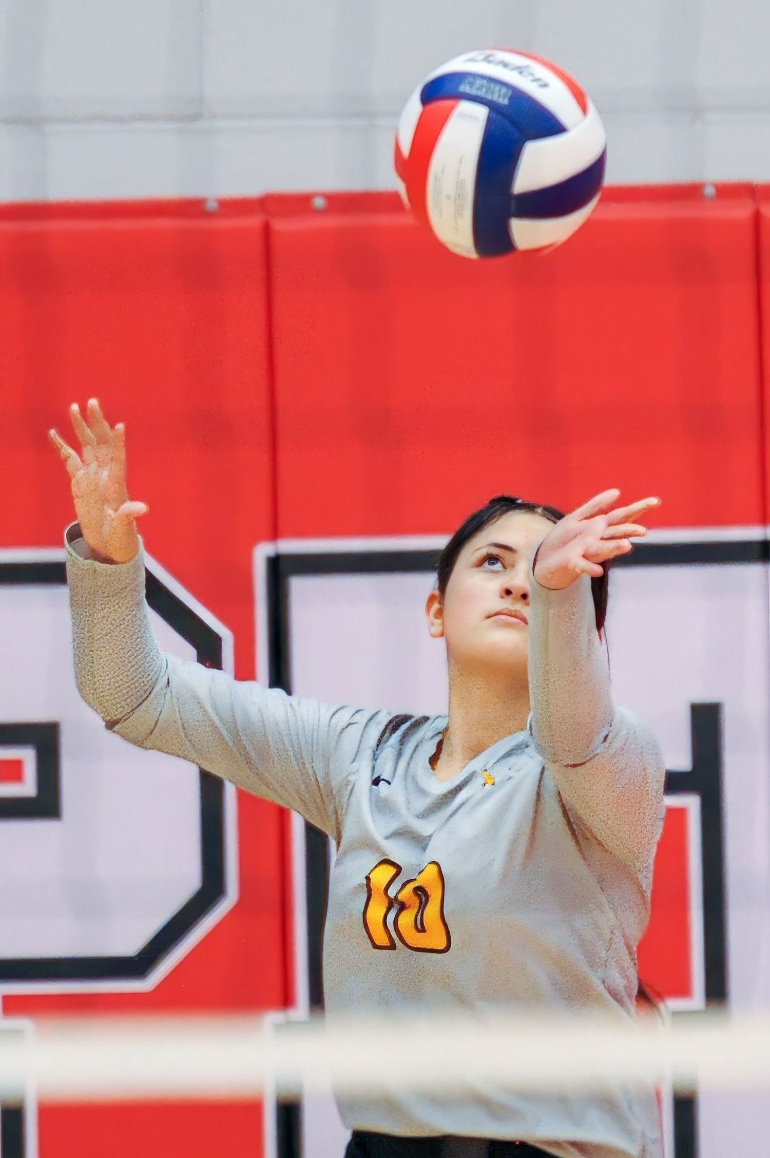 Female volleyball player in gray jersey number 10 preparing to serve ball during indoor match.