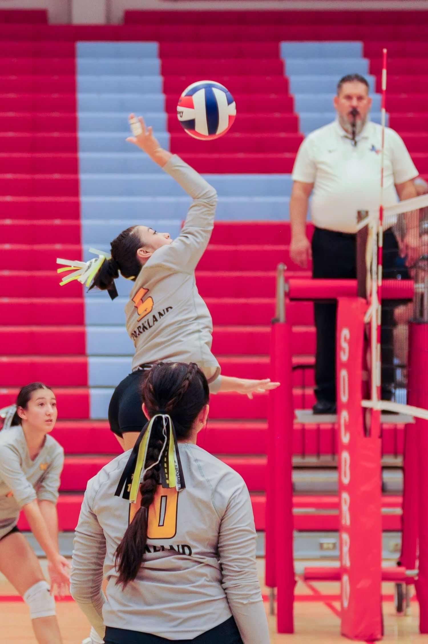 Oakland volleyball player jumps to spike the ball over the net during a competitive indoor match.