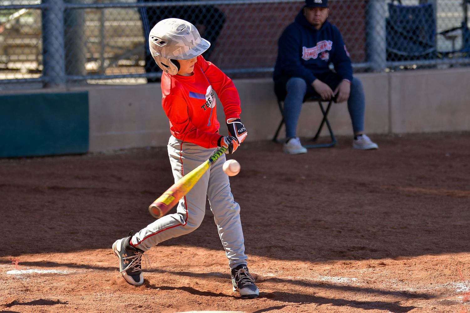 Young boy in red uniform swinging a yellow bat at a baseball during a little league game.