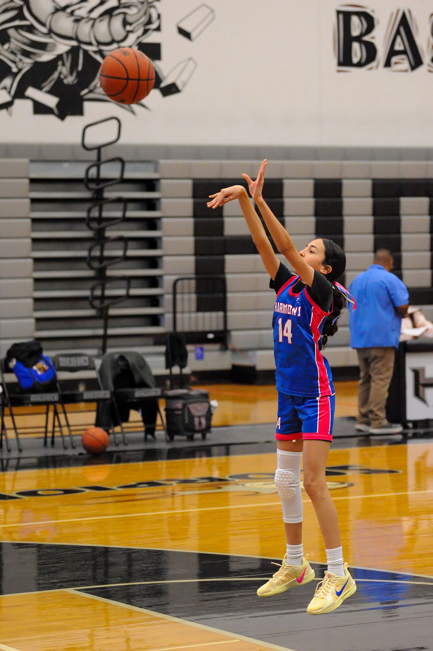 Female basketball player #14 in blue uniform jumps to shoot during an indoor high school game.