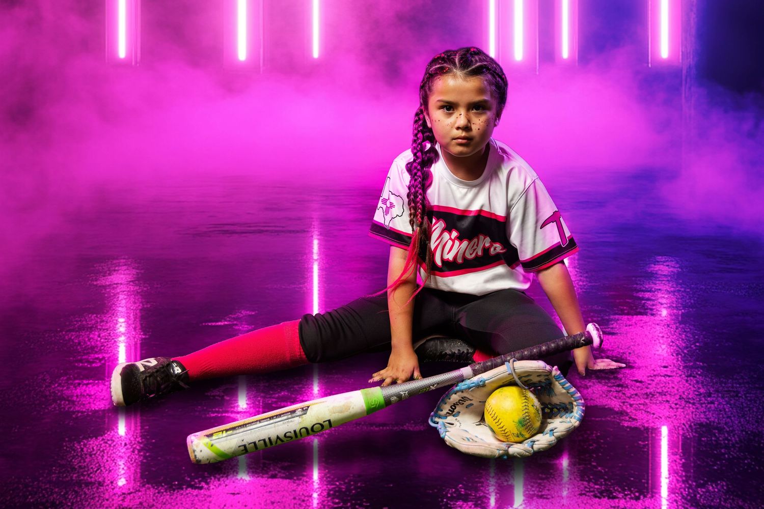 Young girl in softball uniform sits with bat and glove against vibrant pink neon background.