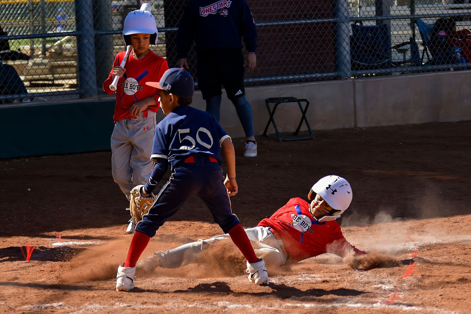 Little league player slides home as fielder number 50 attempts a tag during an exciting play.