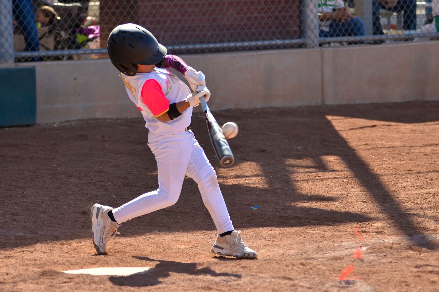 Young baseball player in white uniform makes contact with the ball during a youth league game.