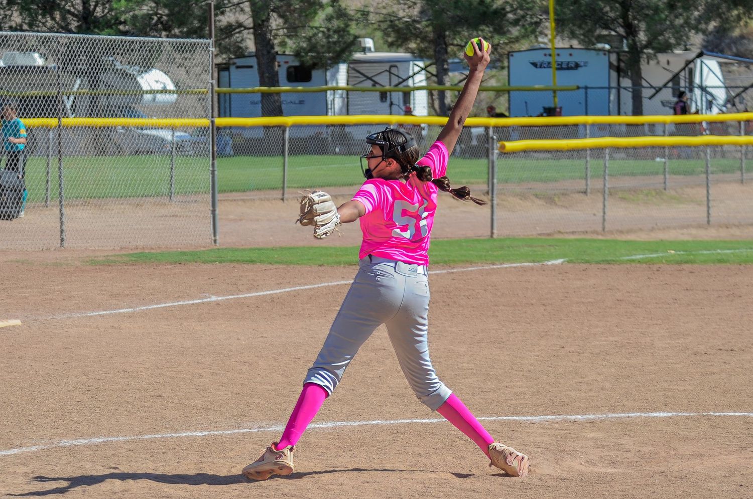 Female softball pitcher in pink uniform and pink socks winding up to throw during an outdoor game.