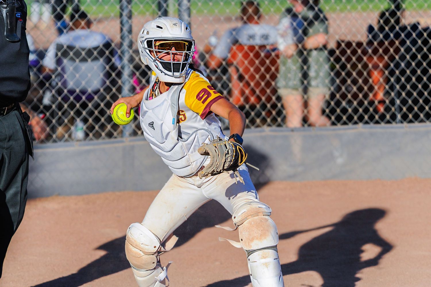 Female softball catcher in white gear catches yellow ball during evening youth league game outdoors.