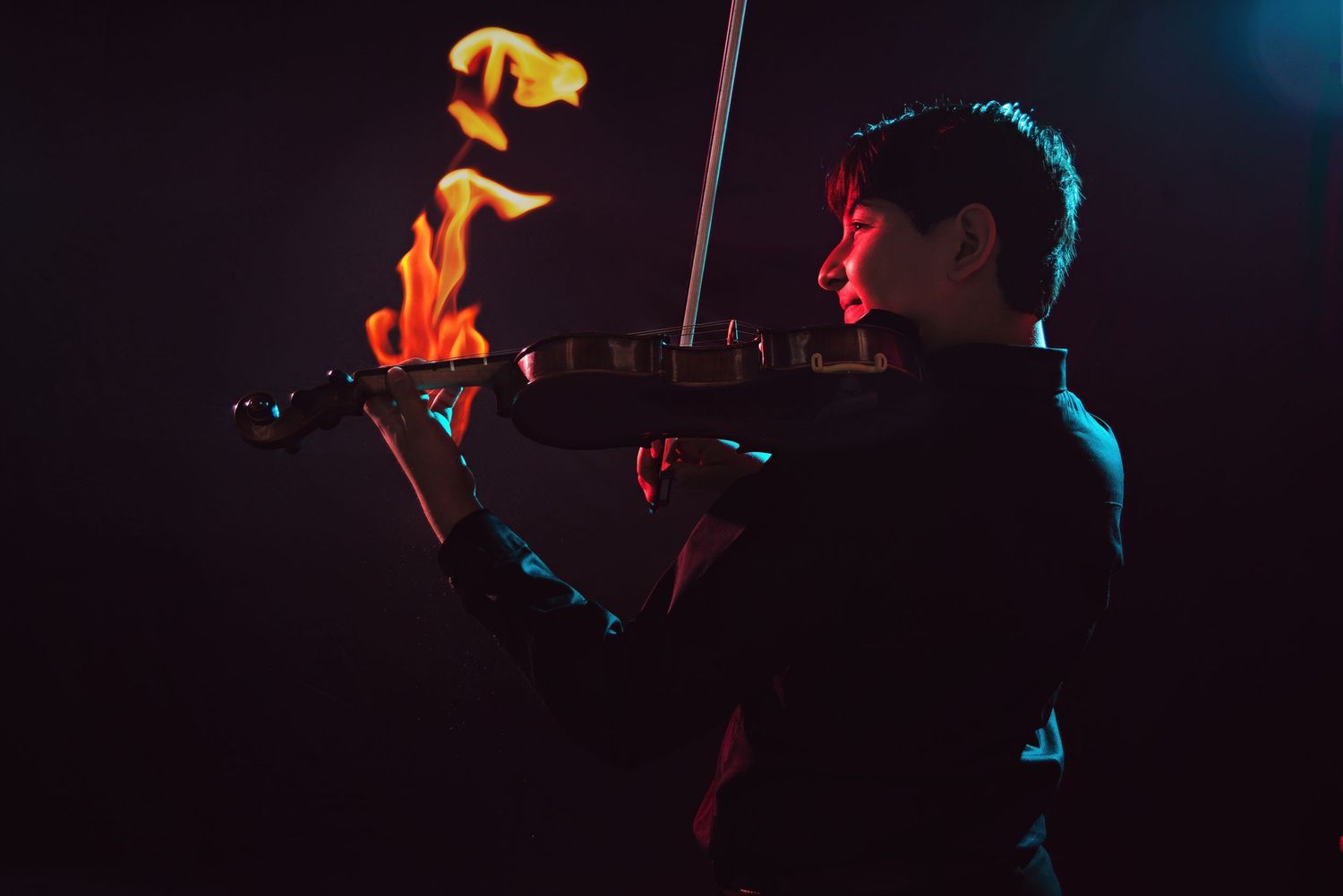 A musician plays violin dramatically with flames rising from the instrument against a dark background.