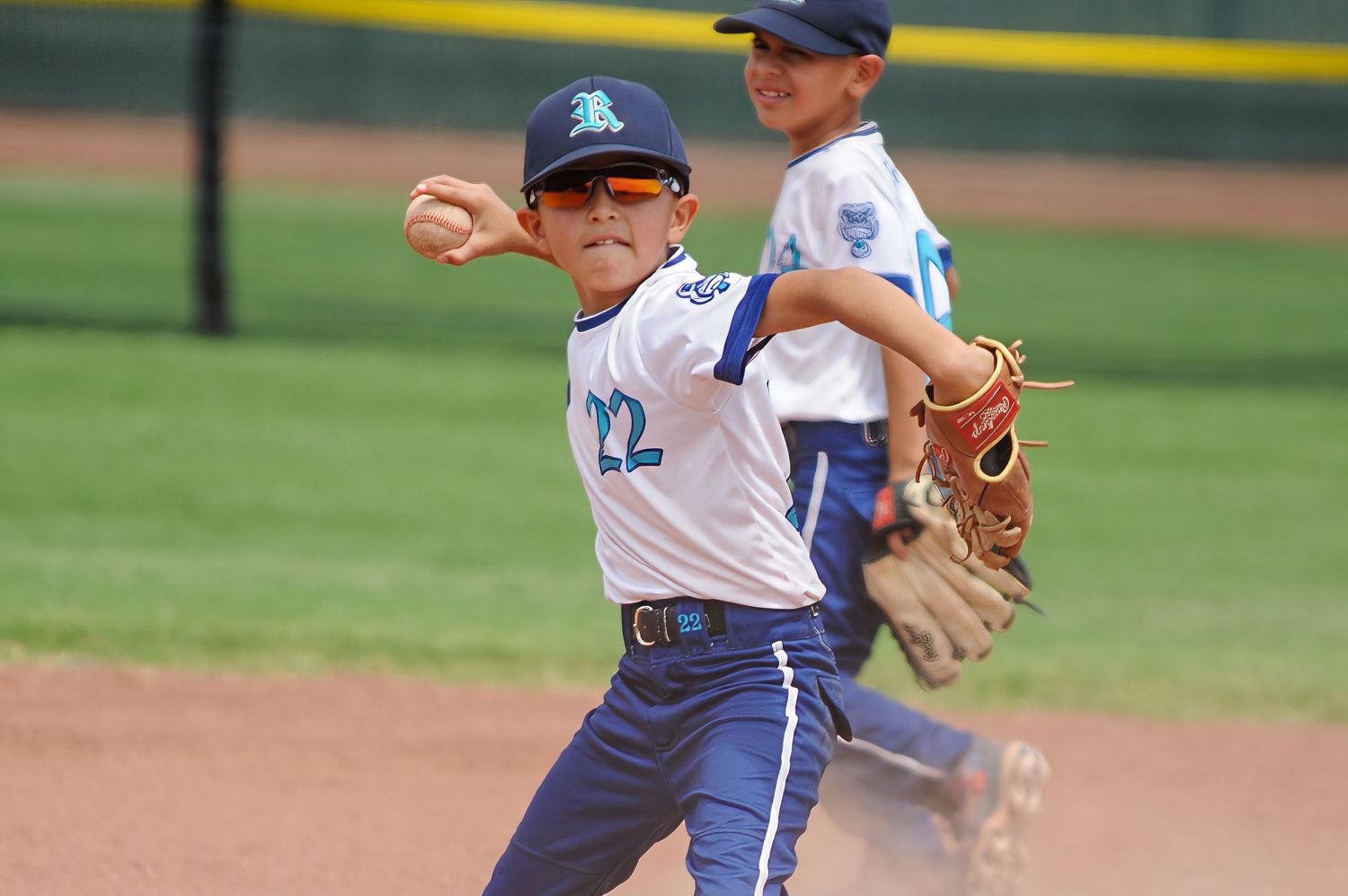 Youth baseball player number 22 in white uniform throwing ball during infield play at youth tournament.