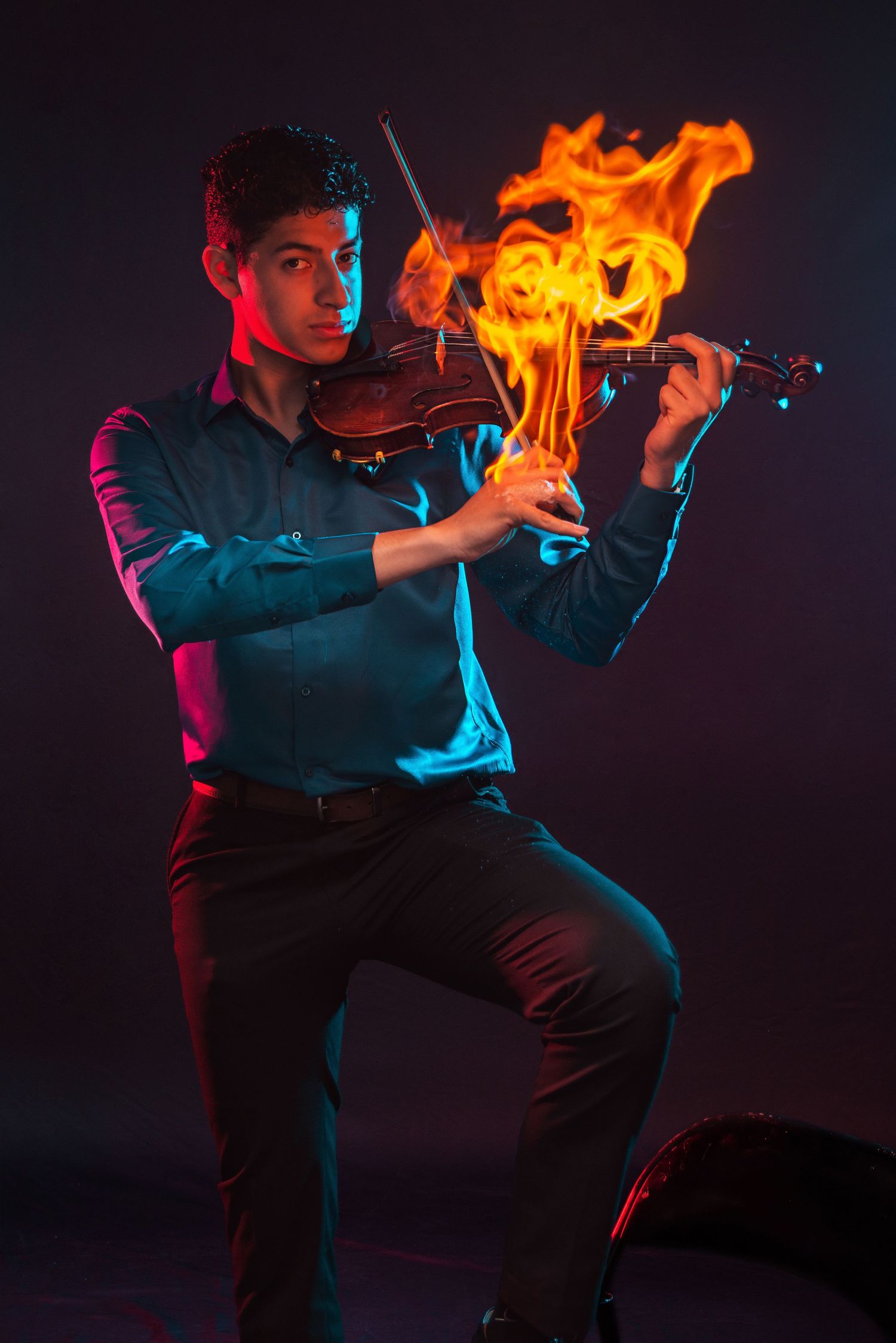 Musician playing a violin engulfed in flames against a dark background with dramatic neon lighting.
