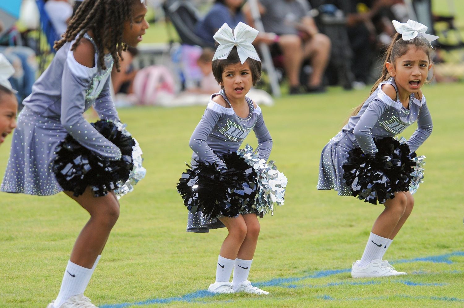 Young girls in matching gray cheerleader uniforms perform with pom-poms on a green field.