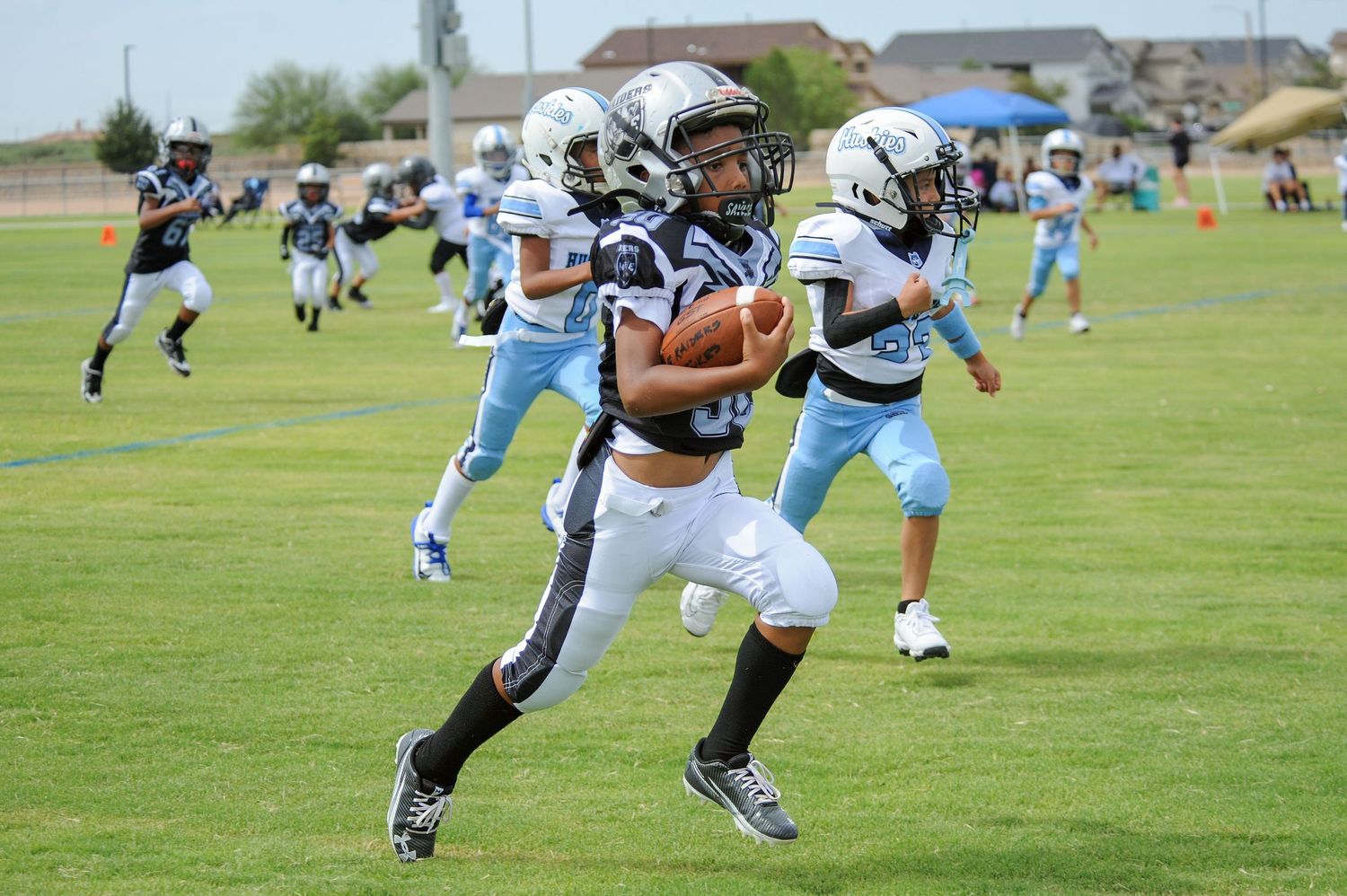 Youth football player in dark uniform runs with ball during a game against light blue team outdoors.