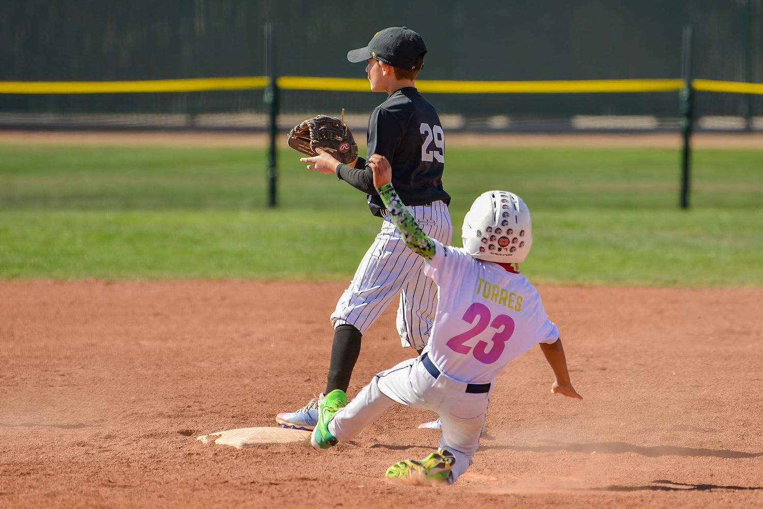 Youth baseball player number 23 slides into second base as fielder attempts to complete the play.