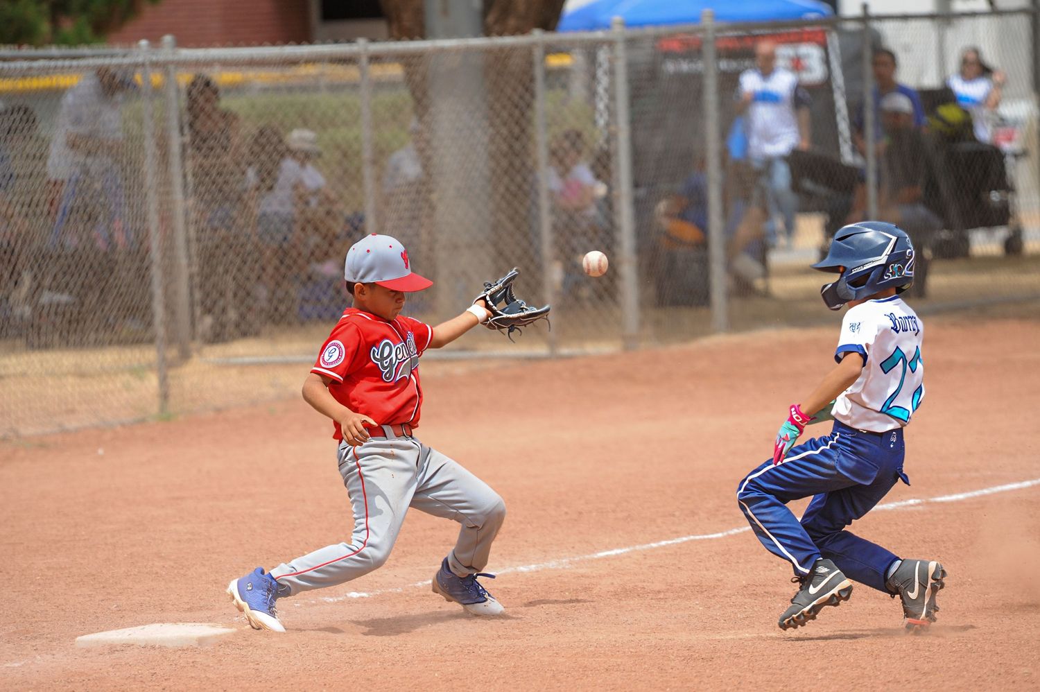 Youth baseball first baseman in red stretches for throw as runner slides in during competitive game.