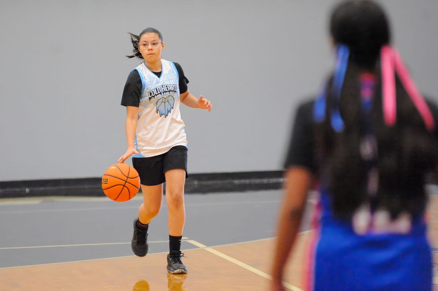 Young female basketball player dribbling ball during indoor practice game on hardwood court.