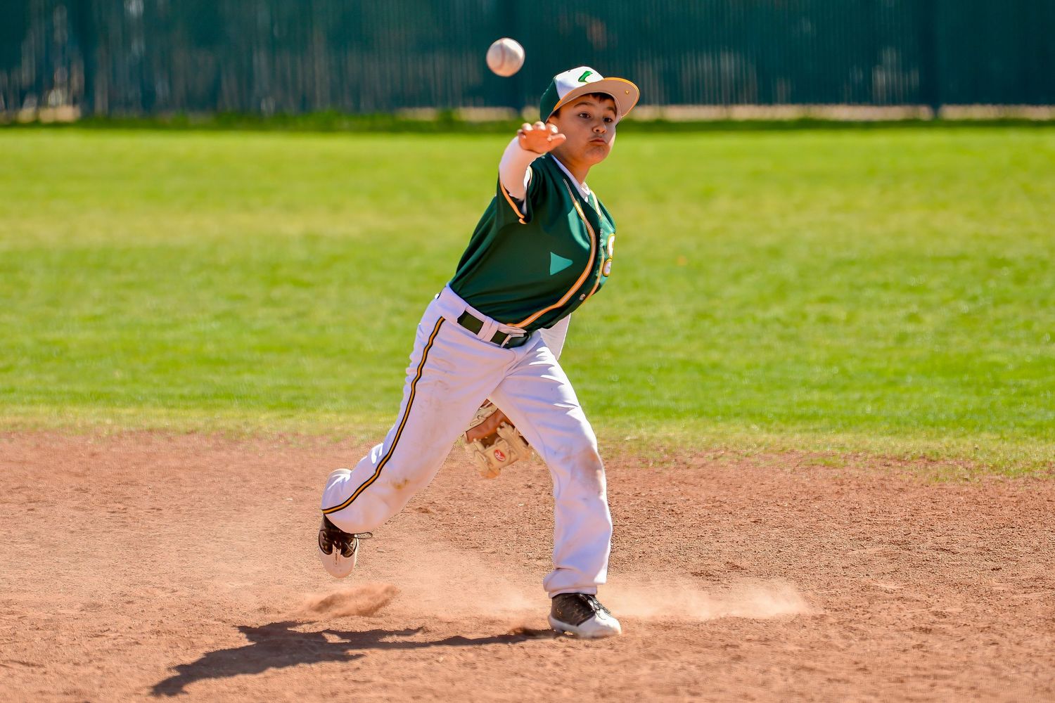 Young pitcher in green uniform delivers a pitch from the mound during a sunny youth baseball game.
